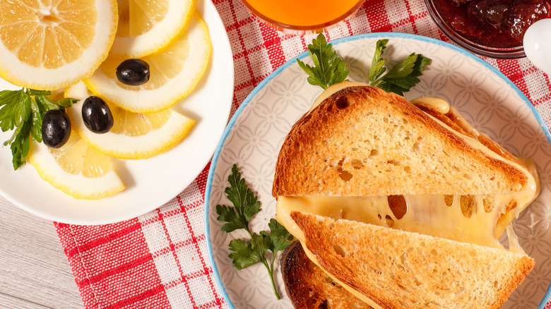 Grilled cheese sandwhich cut across on a plate near lemon slices with olives