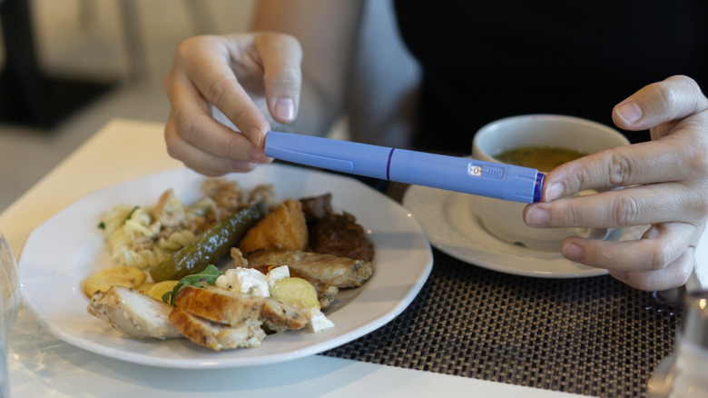A woman holding a container of GLP1, aka Ozempic, in front of coffee and food at a table.