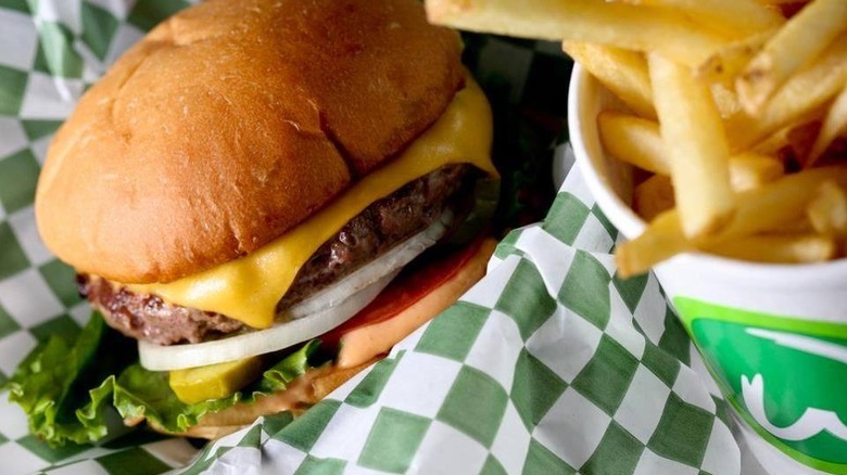 A Wahlburgers cheeseburger topped with government cheese next to a cup of fries
