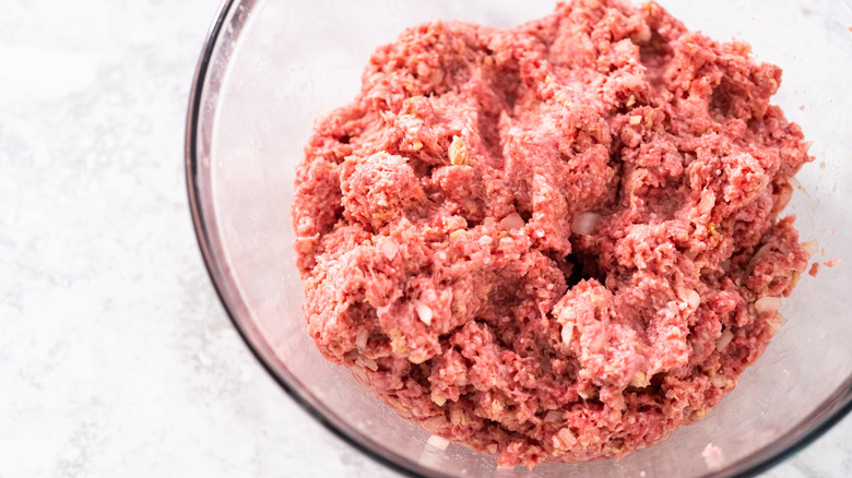 Raw ground meat in a clear bowl with diced onions