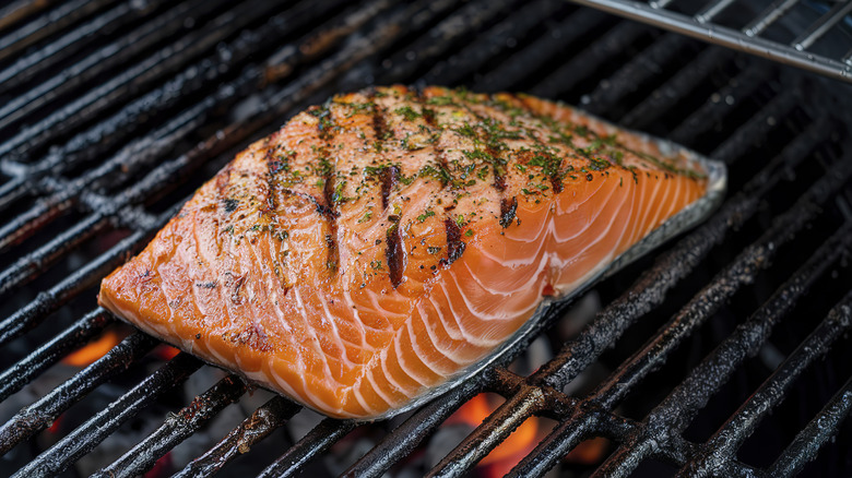 Thawed salmon fillet seasoned with herbs like parsley, grilling over an open flame, with visible char marks.