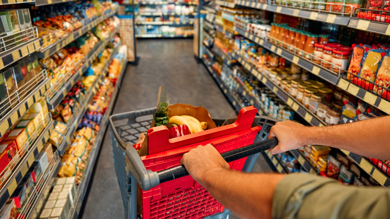 man pushes cart through grocery store aisles