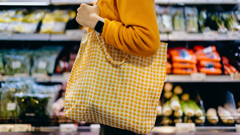 Profile of young woman carrying reusable shopping tote bag in grocery store
