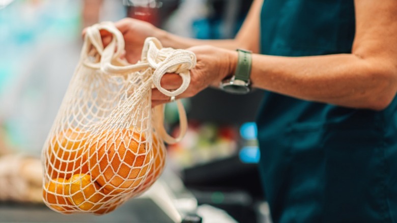 A grocery store checkout clerk with a mesh bag of oranges.