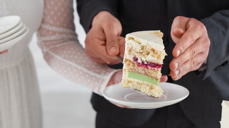 Bride and groom serve a slice of wedding cake on a white plate