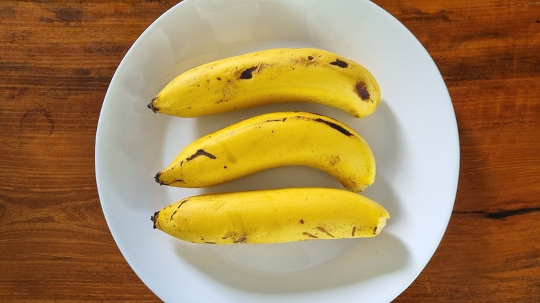 Three bananas on a plate resting on a wooden surface