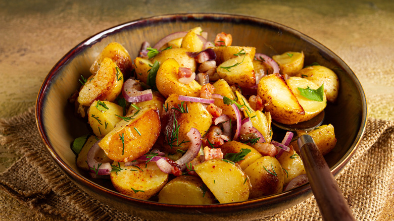 A bowl of German potato salad with onions and cilantro sitting on a brown table.
