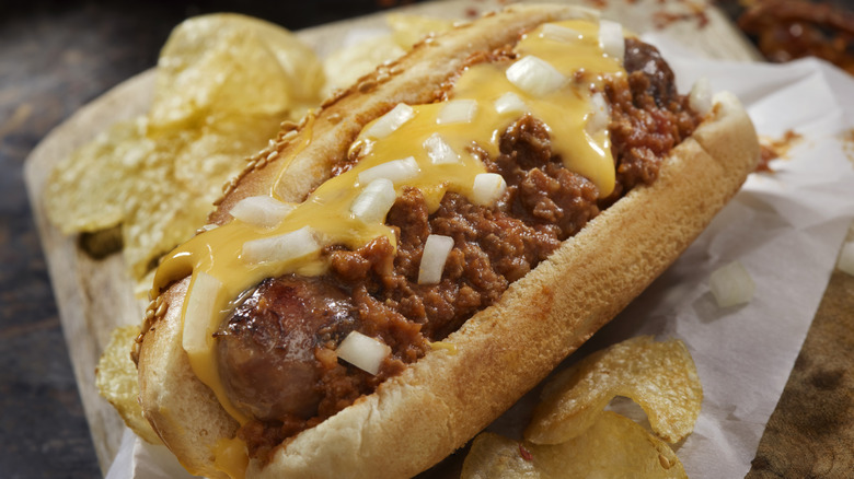 A chili cheese dog with onions and potato chips sitting on a counter