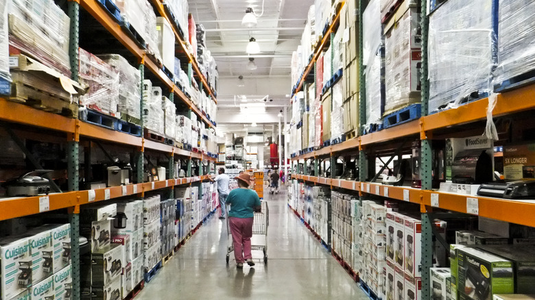 Costco shelves inside a store, with a person's back visible as they walk down an aisle pushing a cart
