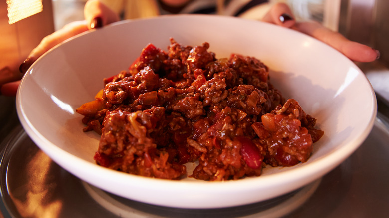 Woman putting leftover chili into microwave oven to cook.
