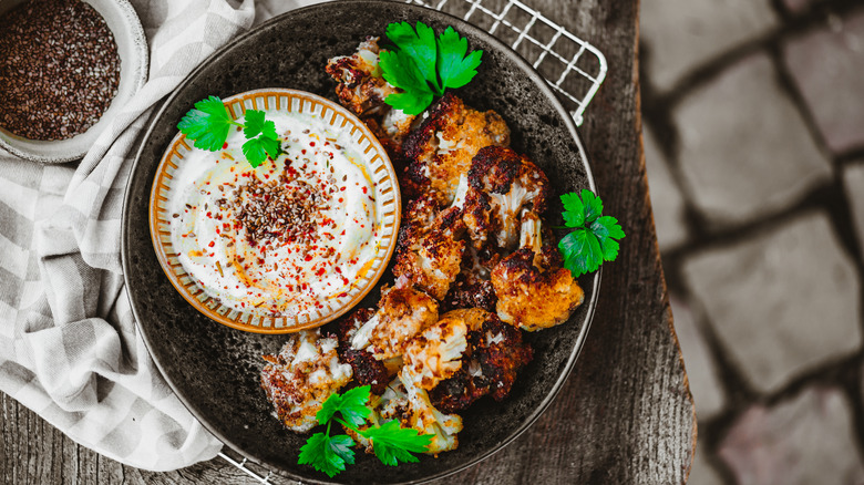 Black plate of roasted cauliflower with white sauce and parsley
