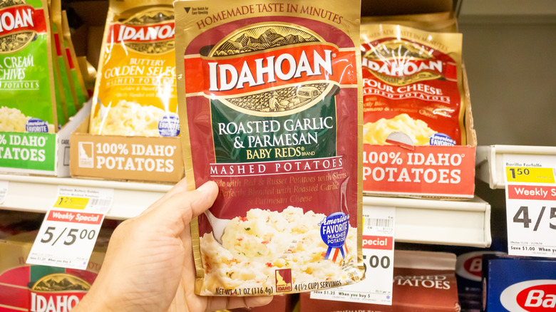 A hand holding a bag of Idahoan roasted garlic and parmesan mashed potatoes in a grocery store aisle