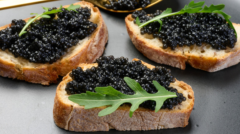 Slices of crusty bread topped with black caviar and leafy greens