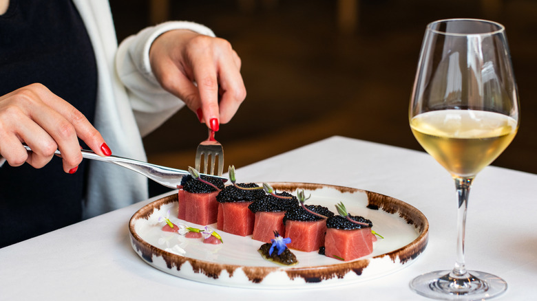 A woman cuts cubes of tuna sashimi with caviar on top