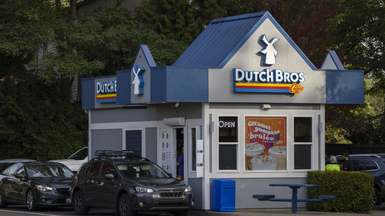 Exterior of a Dutch Bros coffee stand with cars at the drive-thru window