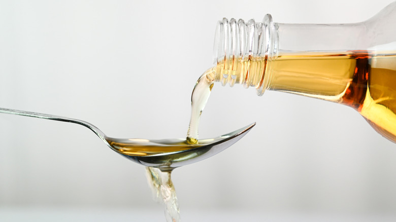 Someone pouring undiluted apple cider vinegar onto an overflowing spoon.