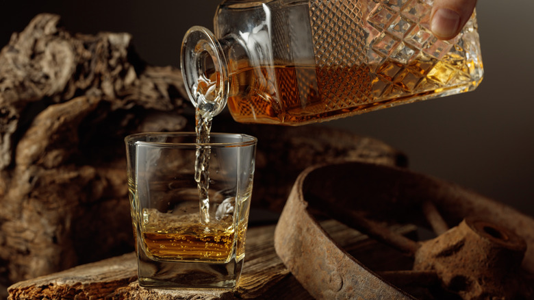 A person pours alcohol from a decanter into a glass