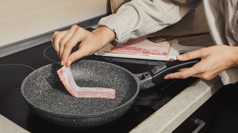hands place raw bacon strip in cold pan