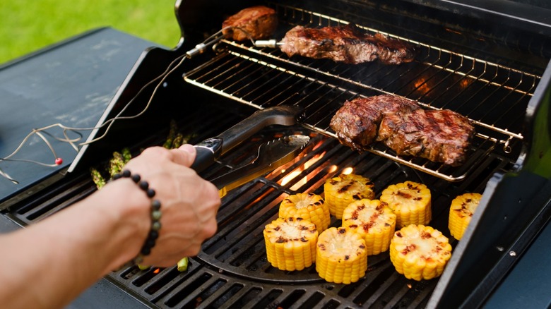 Person grilling steaks and corn