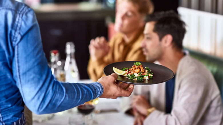 A server bringing a plate of seafood to a table