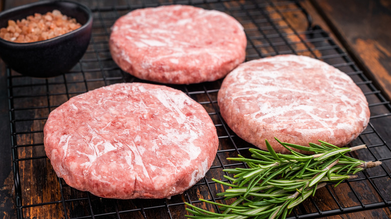Three frozen beef patties on a black wire tray