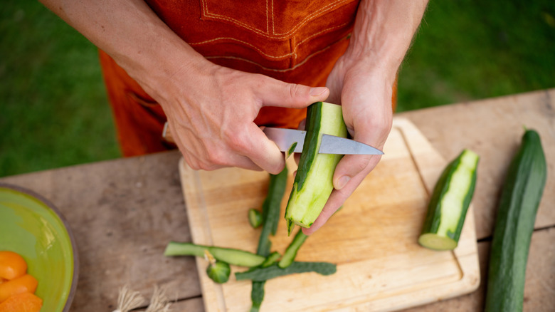 Two hands peeling a cucumber with a large knife