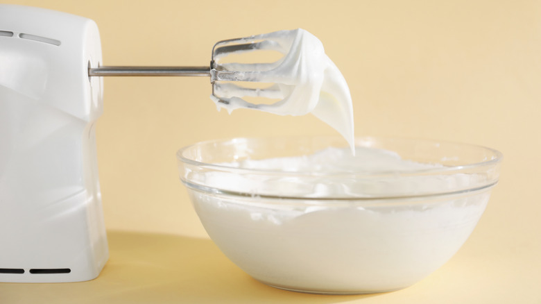 white hand mixer laying down above glass bowl of whipped cream