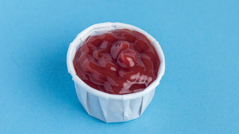 A paper container filled with ketchup on a blue background