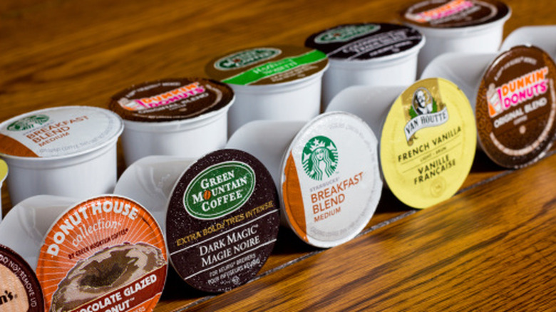 Various K-Cup pod flavors lined up on a wood table.