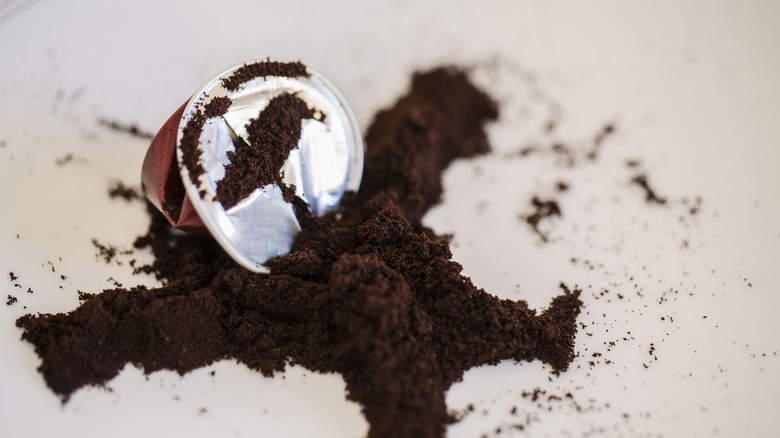 An opened coffee pod with coffee grounds spilled out in a pile.