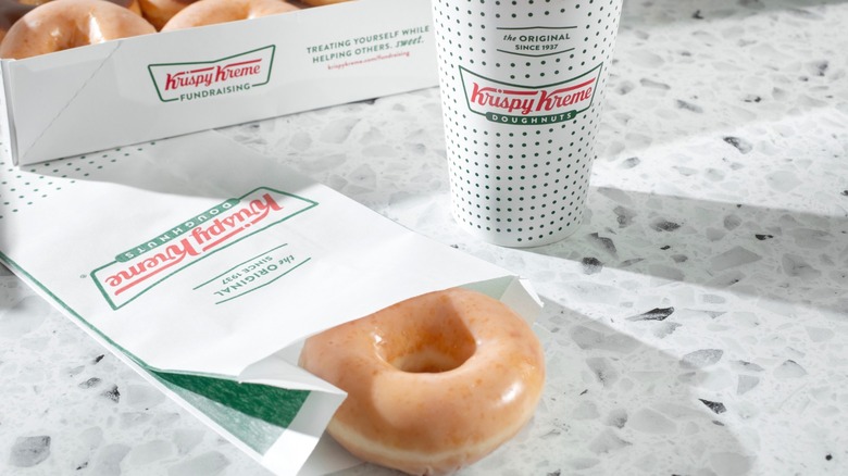 A Krispy Kreme doughnut and coffee on a table.