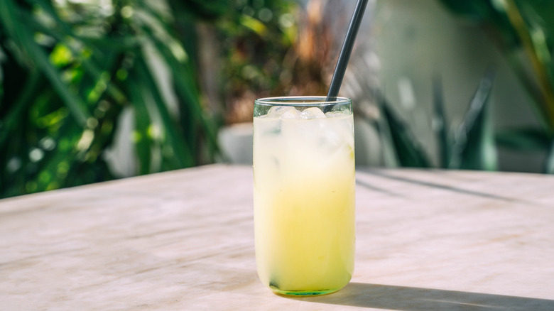 A glass full of lemonade and ice on a table outside