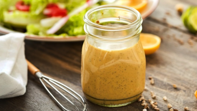 A jar of homemade salad dressing with salad in the background.