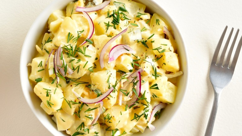 Bowl of mustard potato salad with fresh herbs and sliced red onions.