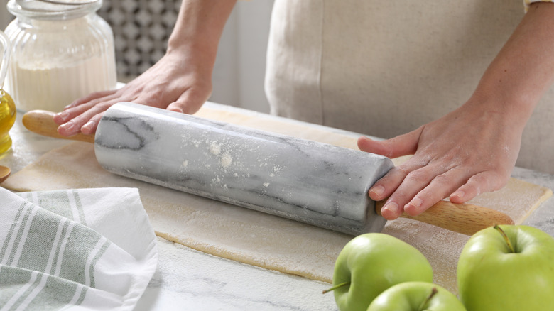 Hands rolling out dough with marble rolling pin alongside green apples