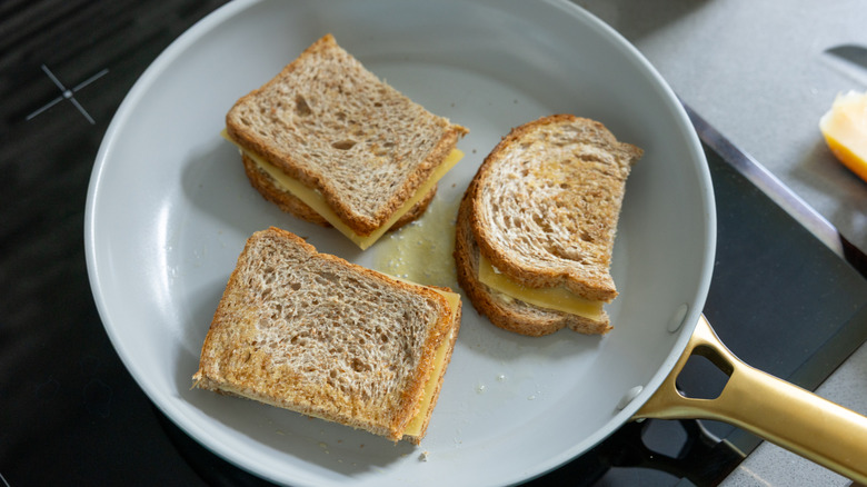 Three grilled cheese sandwiches cooking in a skillet