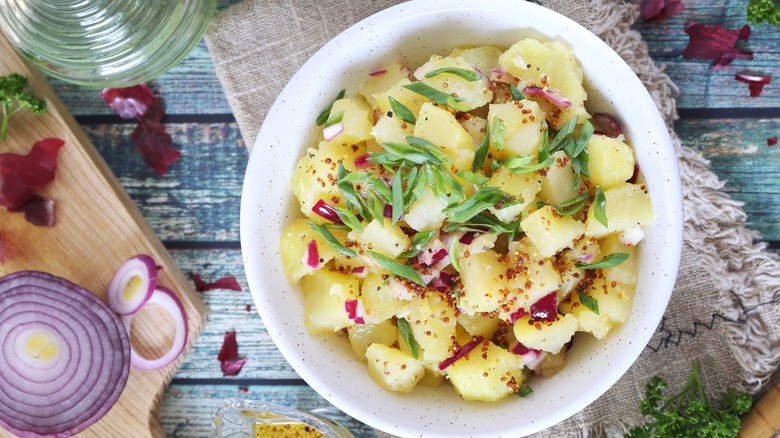 Potato salad dressed with vinaigrette in white bowl on a farmhouse table.