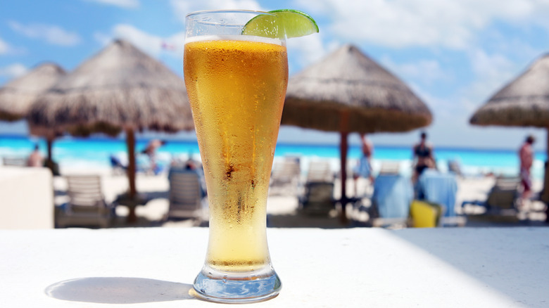tall beer glass covered in condensation with lime at resort with palapas in the background