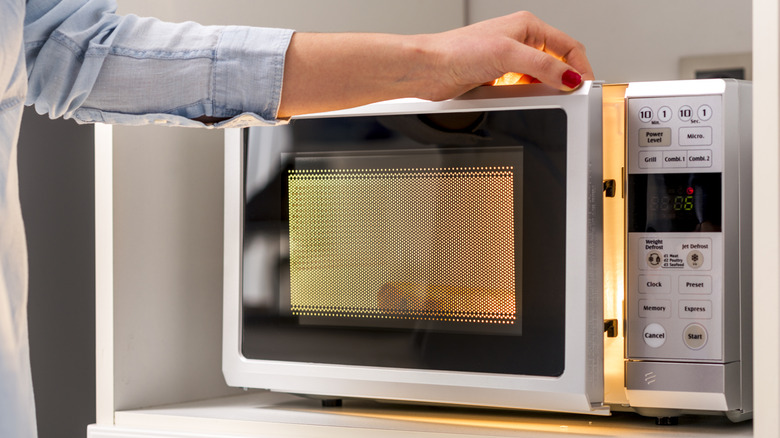 A woman opens the door of an illuminated microwave