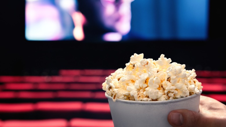 A person in a movie theater holding a bucket of popcorn.