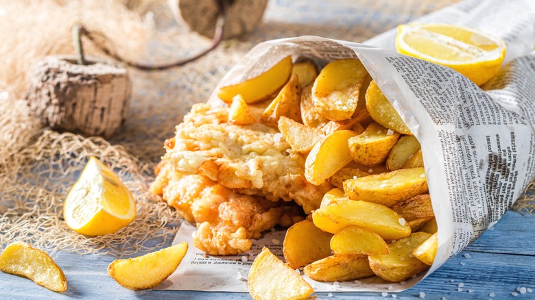 A close-up of fish and chips served in a newspaper cone with slices of lemon.