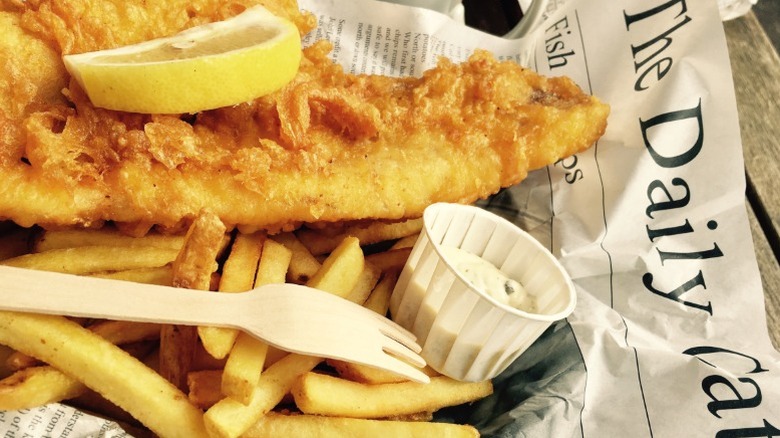 Fish and chips served on newspaper, with lemon and tartar sauce.
