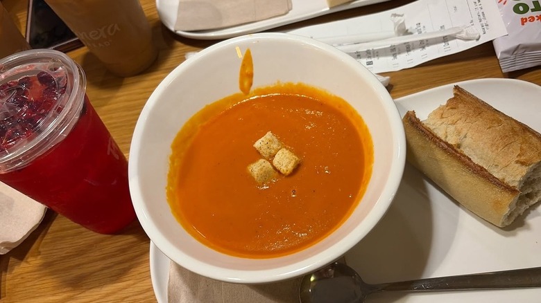 Bowl of tomato soup with croutons, baguette, and drink from Panera