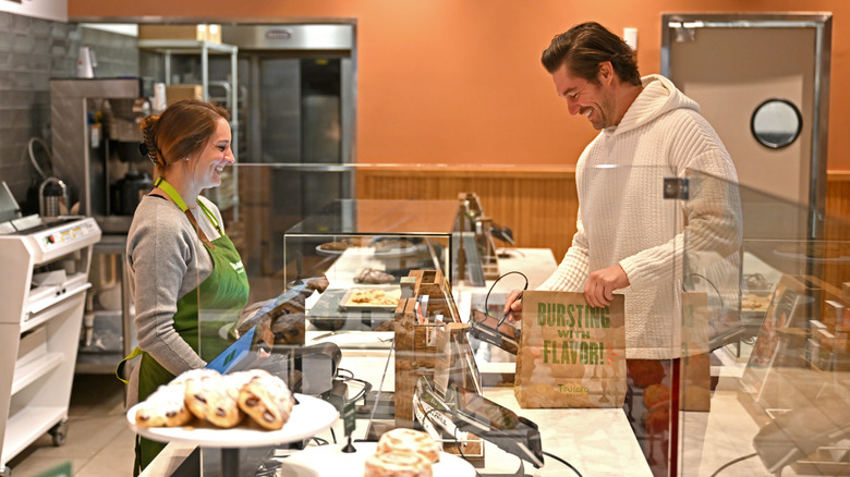 A man buying something at Panera Bread while employee smiles behind the counter