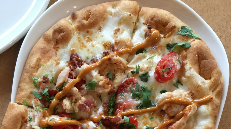 Panera flatbread pizza or Crispani on a plate with tomatoes, herbs, cheese, and sauce drizzle