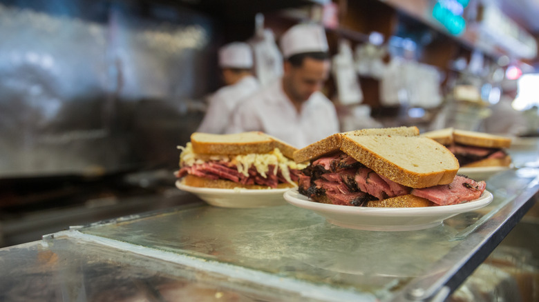 Pastrami sandwiches on deli counter with cooks in background