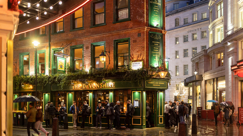 People drinking outside a brightly-lit pub in London in the evening