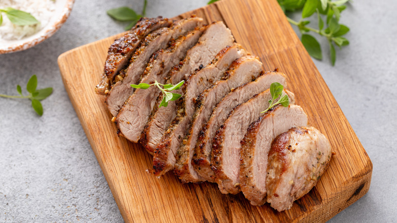 Sliced cooked pork on a wooden board garnished with greens
