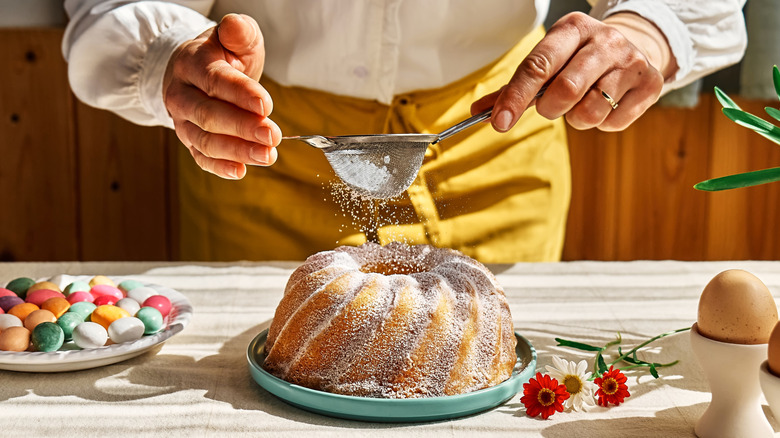hands sifting powdered sugar over a Bundt cake