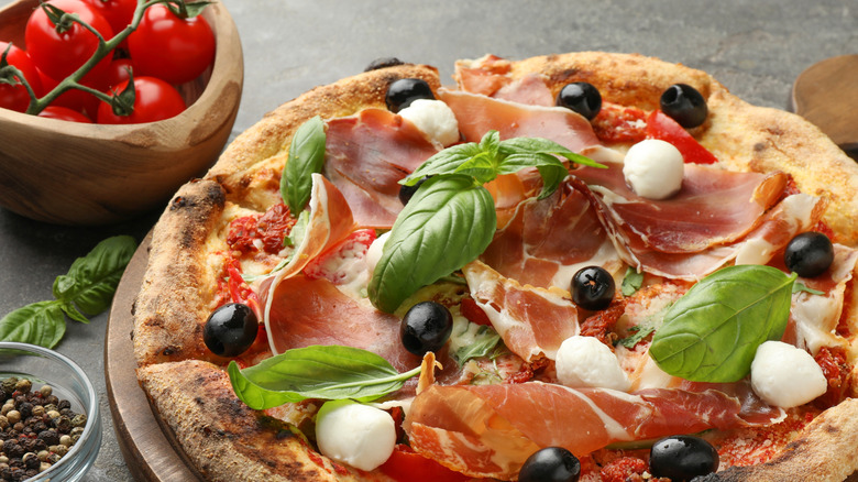 Homemade pizza with basil, prosciutto crudo, mozzarella, and olives
